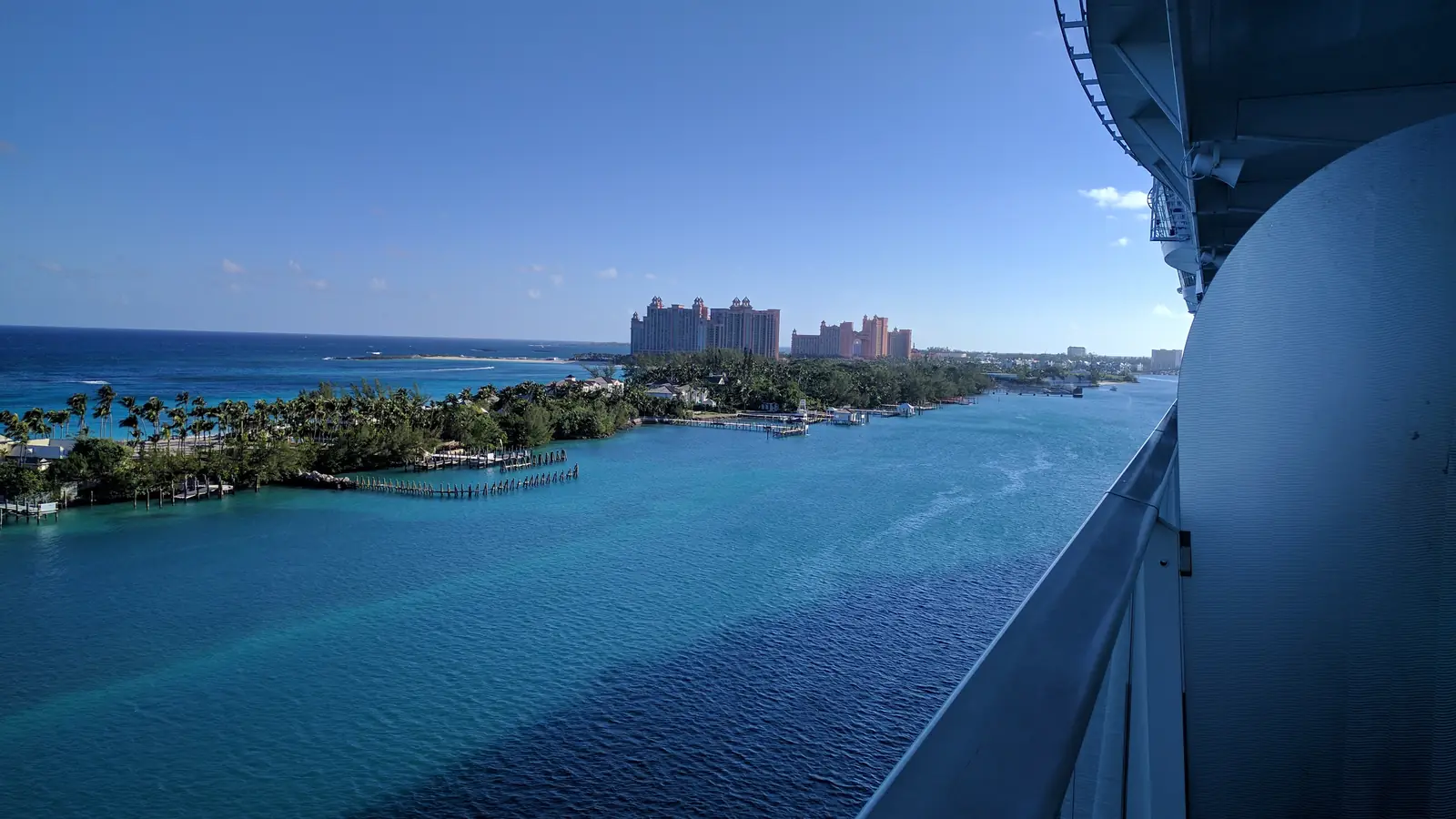 Turquoise Caribbean water seen from a cruise ship balcony, with a palm-lined shore in the distance