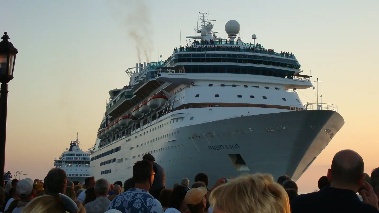 A crowd on the dock watching a cruise ship at sunset