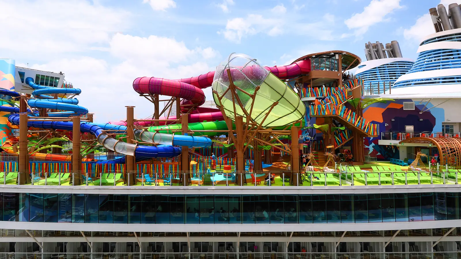Colorful waterslides and a climbing wall on the top deck of a large cruise ship